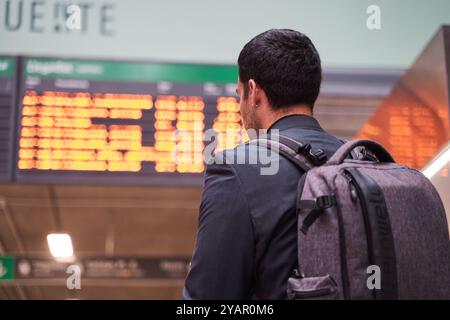Stilvoller junger Geschäftsmann, der sich den Flugplan ansieht. Nicht erkennbarer Mann mit Reiserucksack Stockfoto