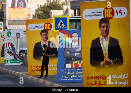Duhok, Irak. Oktober 2024. Ein junger Mann steht neben Wahlbändern der Kandidaten der Kurdischen Demokratischen Partei (KDP/PDK) und anderer, die Bilder des Vizepräsidenten der Partei Nechirvan Barzani vor den Wahlen zum Kurdischen Regionalparlament in Duhok, Irak, tragen. (Foto: Ismael Adnan/SOPA Images/SIPA USA) Credit: SIPA USA/Alamy Live News Stockfoto