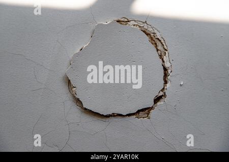 Nahaufnahme einer gerissenen Wand mit abblätternder Farbe und freiliegenden Schichten, die auf strukturelle Schäden oder Verschlechterungen im Laufe der Zeit hinweisen Stockfoto