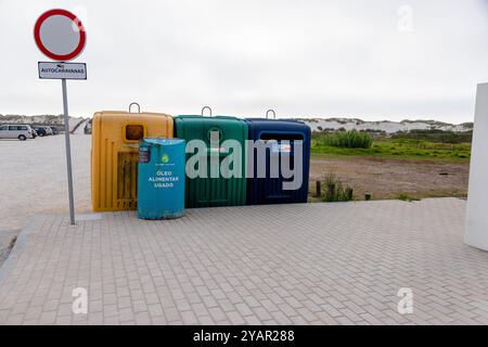 Ein Satz farbenfroher Recyclingbehälter, einschließlich Behälter für Glas, Papier, Plastik und gebrauchtes Speiseöl, in der Nähe eines Sandstrandes Stockfoto