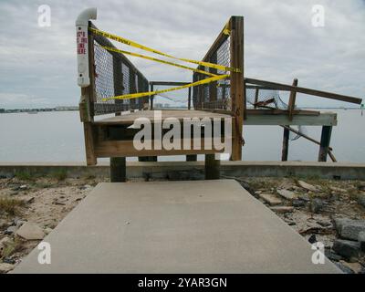 Vordere POV führende Linien gelbes Klebeband Warnansicht beschädigte hölzerne Beach Access Bridge am späten Nachmittag. Gulfport Florida Beach. Gehsteig aus Beton und Sand Stockfoto