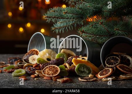 Getrocknete tropische Früchte mit verschiedenen Nüssen und Rosinen in kleinen Metalleimern. Süße tropische Früchte und Weihnachtsbaum auf einem Küchentisch. Stockfoto
