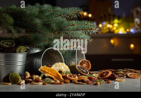 Getrocknete tropische Früchte mit verschiedenen Nüssen und Rosinen in kleinen Metalleimern. Süße tropische Früchte und Weihnachtsbaum auf einem Küchentisch. Stockfoto
