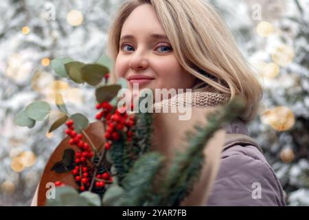 Weibliches Porträt mit Weihnachtsstrauß. Junge Frau in warmen Kleidern auf dem Hintergrund von verschneiten Bäumen. Stockfoto