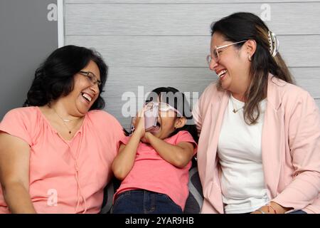 Latina Brünette Großmutter, Mutter und Tochter benutzen ihr Handy, um einzukaufen, Filme zu sehen, Videoanrufe zu tätigen und im Wohnzimmer zu spielen Stockfoto
