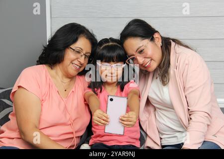 Latina Brünette Großmutter, Mutter und Tochter benutzen ihr Handy, um einzukaufen, Filme zu sehen, Videoanrufe zu tätigen und im Wohnzimmer zu spielen Stockfoto