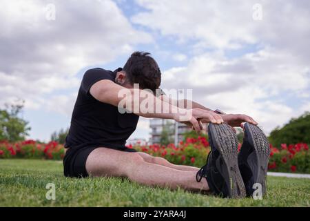 Mann sitzt auf dem Gras in einem Park und streckt seine Beine nach einem Workout. Konzept eines gesunden Lebensstils Stockfoto