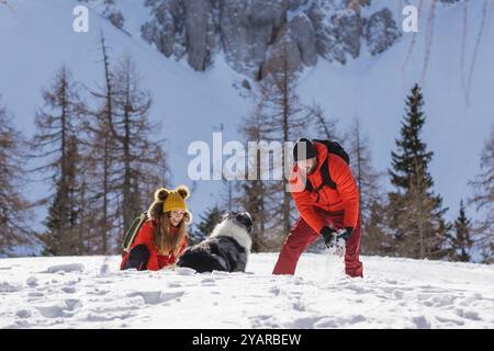 Das Paar spielt im Winter mit seinem Haustier mit Bergkulisse gerne mit Schnee Stockfoto