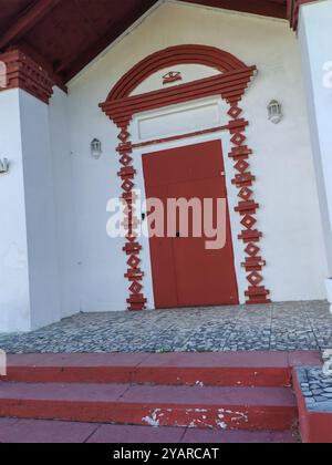 Kleines weißes Gebäude mit roten Akzenten und einem Eingang mit Mosaikfliesen und einem dekorativen Pflanzgefäß davor. Die charmante Fassade spiegelt traditionell wider Stockfoto