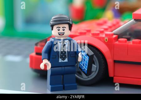 Tambow, Russische Föderation - 15. Oktober 2024 Eine Minifigur eines Lego-Geschäftsmannes, die vor seinem Lego Ferrari F40 steht und ein Handy hält. Stockfoto