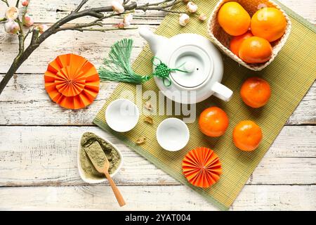 Teekanne mit Mandarinen, Schüssel mit gepudertem Matcha-Tee, blühender Sakura-Zweig und orientalischen Symbolen auf weißem hölzernem Hintergrund. Neujahrsfeier Stockfoto