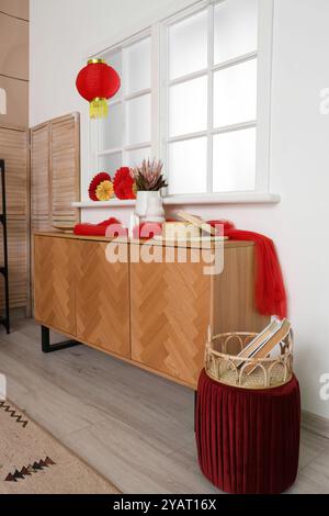 Holzschrank mit traditioneller chinesischer Dekoration in der Nähe des Fensters im Wohnzimmer. Chinesisches Neujahrsfest Stockfoto