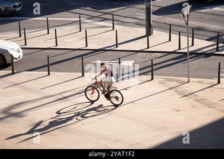 Belgrad, Serbien - 10. Oktober 2024: Frau, die an einem sonnigen Morgen auf dem Bürgersteig der Stadt mit Verkehrspollern Fahrrad fährt Stockfoto