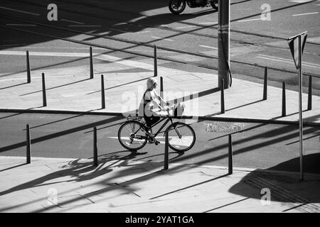 Belgrad, Serbien - 10. Oktober 2024: Frau, die an einem sonnigen Morgen an einer Straßenkreuzung mit Verkehrspollern Fahrrad fährt, in kontrastreichem Schwarz Stockfoto