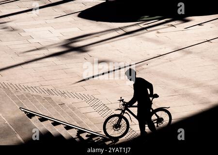 Belgrad, Serbien - 10. Oktober 2024: Schattensilhouette einer Person, die ein Fahrrad auf einer Radtreppenrampe nach oben schiebt, in kontrastreicher Schwarz-weiß-Optik Stockfoto