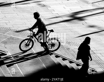 Belgrad, Serbien - 10. Oktober 2024: Schattensilhouette einer Person, die ein Fahrrad auf einer Radtreppenrampe hochschiebt, und einer Frau, die in der Höhe hinuntergeht Stockfoto