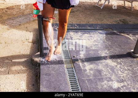 Frau, die nach dem Tag Sandfüße unter der Stranddusche auf Sand spülte. Curacao. Stockfoto