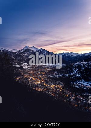 Ein Panoramablick auf das Skigebiet Serre Chevalier Valley in den französischen Alpen in der Abenddämmerung. Die schneebedeckten Berge umgeben das beleuchtete Tal als Himmel Stockfoto