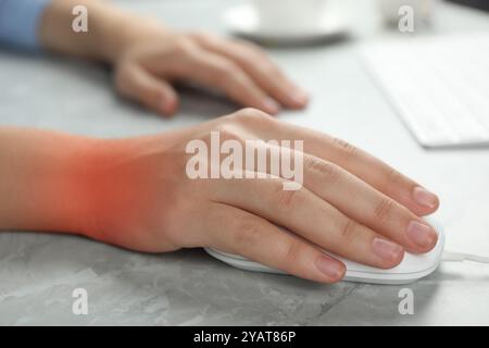 Frau, die an Schmerzen im Handgelenk leidet, während sie Computermaus am grauen Tisch benutzt, Nahaufnahme. Büroarbeit, Karpaltunnelsyndrom Stockfoto