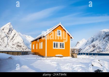 Traditionelles gelbes Rorbu-Haus und der Berg Olstind im Fischerdorf Sakrisoy auf den Lofoten-Inseln in Norwegen. Winterlandschaft mit schneebedeckten Bergen Stockfoto