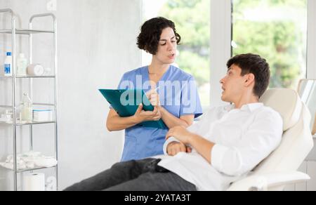 Ärztin kommuniziert mit männlichen Patienten in der kosmetologischen Klinik vor der Operation Stockfoto