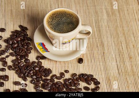 Tasse Kaffee im Vordergrund mit gerösteten Kaffeebohnen mit hellem mattem Hintergrund Stockfoto