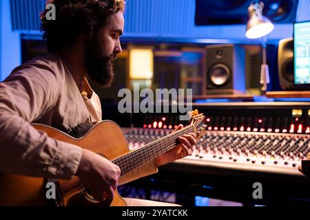 Komponist, der elektroakustische Gitarrenklänge spielt, um mit seinem Produzenten im Musikstudio einen neuen Song aufzunehmen und im Kontrollraum die Titel zu bearbeiten. Der Künstler spielt Live-Auftritte mit Instrument. Stockfoto