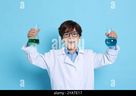 Junge mit Glaswaren, der vorgibt, Wissenschaftler zu sein, auf hellblauem Hintergrund. Träumen vom zukünftigen Beruf Stockfoto