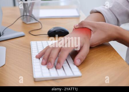 Mann mit Schmerzen im Handgelenk am Holztisch, Nahaufnahme. Büroarbeit, Karpaltunnelsyndrom Stockfoto