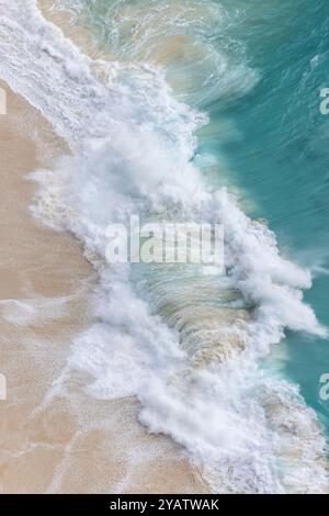 Von oben krachen türkisfarbene Wellen sanft auf den weichen Sand von Kelingking Beach in Nusa Penida, Bali. Die hellen Farben zeigen die Schönheit und Ruhe Stockfoto