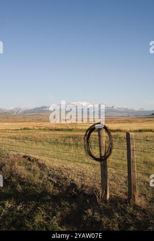 Eine Rolle alten rostigen Stacheldrahts hängt an der Zaunpfosten-Spitze. Entsorgter Draht aus der Reparatur von Zaunen ist gefährlich für Tiere und Ausrüstung. Teton County, MT. Stockfoto