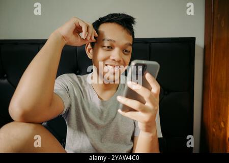 Ein Mann lächelt, während er das Smartphone auf dem Bett hält Stockfoto