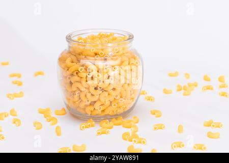 Ungekochte Chifferi Rigati Pasta in Glasglas auf weißem Hintergrund. Fett und ungesunde Lebensmittel. Verstreute Klassische Trockene Makkaroni. Italienische Kultur und Küche. Rohe Pasta Stockfoto