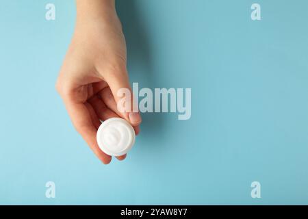 Nahaufnahme der Frauenhände, die eine Flasche weiße Gesichtscreme auf grauem Hintergrund halten. Hautpflege. Draufsicht Stockfoto