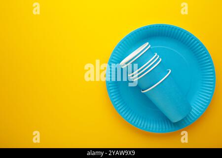 Umweltfreundliche Einweg-Utensilien aus Bastelpapier auf gelbem Hintergrund. Blaue Teller und Pappbecher. Draufsicht Stockfoto