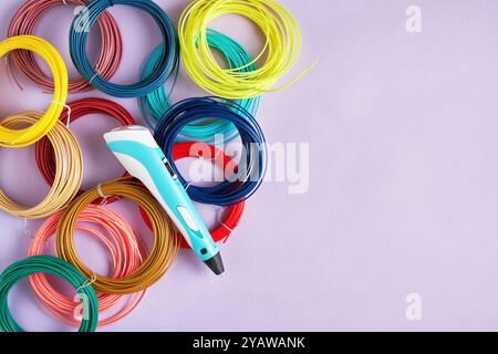 Der 3D-Druckstift liegt auf einer violetten Oberfläche, umgeben von farbenfrohen Filamentspulen. Perfekt für Projekte im Zusammenhang mit Handwerk, Technologie oder Heimwerkern Stockfoto