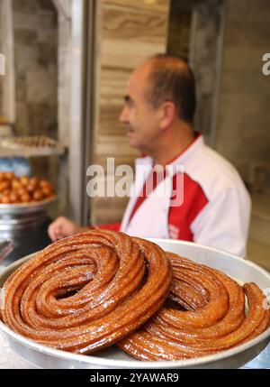 ADANA, TÜRKEI - 23. OKTOBER 2018: Mitarbeiter eines unbekannten Dessertgeschäfts, der auf den Verkauf des traditionellen Adana Desserts Sari Burma aka türkischer Churro wartet Stockfoto