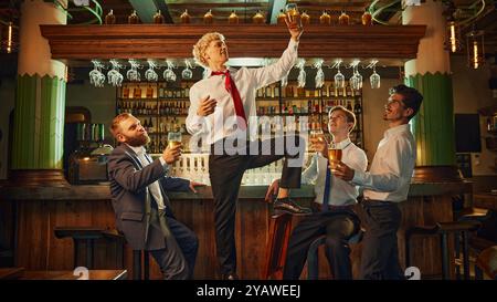 Eine Gruppe von Männern entspannen sich an der Bar, unterhalten sich lebhaft und lachen, während sie ihre Drinks genießen und die Kameradschaft fördern. Stockfoto