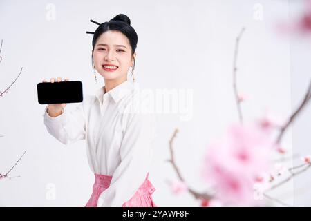 Eine junge Chinesin, die ein Telefon hält und in die Kamera schaut Stockfoto
