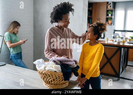 Glückliche alleinerziehende schwarze Mutter und Kind, die Hausarbeiten erledigen, Kind, das zu Hause Smartphone benutzt Stockfoto