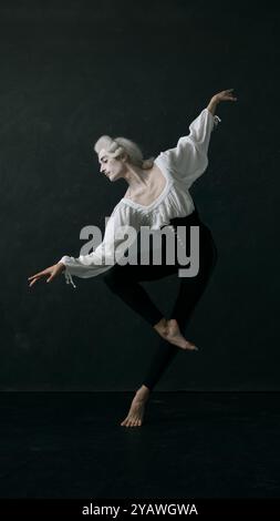 Dynamisches Porträt einer jungen Balletttänzerin, die alte Kleidung und Perücke kleidet und anmutig in Bewegung vor Vintage-Hintergrund hüpft. Stockfoto