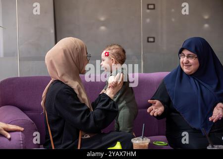 Zwei Frauen in Hijabs und ein Kind, das zusammen in einem Café sitzt, Gespräche teilt und Kaffee genießt. Die Szene zeigt ein warmes, familienfreundliches Atmosp Stockfoto