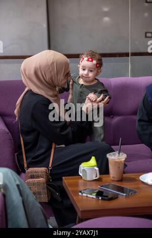 Zwei Frauen in Hijabs und ein Kind, das zusammen in einem Café sitzt, Gespräche teilt und Kaffee genießt. Die Szene zeigt ein warmes, familienfreundliches Atmosp Stockfoto