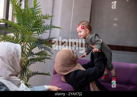 Zwei Frauen in Hijabs und ein Kind, das zusammen in einem Café sitzt, Gespräche teilt und Kaffee genießt. Die Szene zeigt ein warmes, familienfreundliches Atmosp Stockfoto