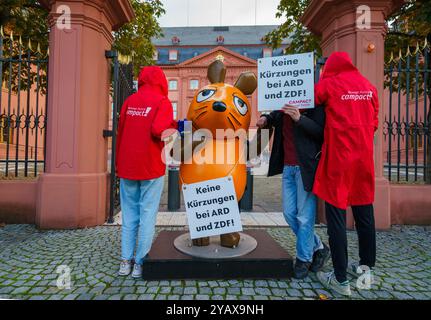 16. Oktober 2024, Rheinland-Pfalz, Mainz: Die Figur der Maus aus der Sendung mit der Maus steht zwischen Aktivisten der Kampagne vor dem Rheinland-pfälzischen landtag mit Schildern mit der Aufschrift „keine Kürzungen an ARD und ZDF!“. Aktivistinnen und Aktivistinnen des „Campact e.V.“ sind mit der entführten „Maus“ vor dem ZDF und dem landtag in der Landeshauptstadt erschienen. Die Aktivisten wollen die Aufmerksamkeit auf den Wert des öffentlich-rechtlichen Rundfunks lenken. Jahrelang schmückte die Skulptur der Kultfigur aus der Sendung mit der Maus das vierteilige Gebäude des Westdeutschen Rundfunks (WDR) in Köln Stockfoto