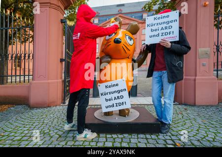 16. Oktober 2024, Rheinland-Pfalz, Mainz: Die Figur der Maus aus der Sendung mit der Maus steht zwischen Aktivisten der Kampagne vor dem Rheinland-pfälzischen landtag mit Schildern mit der Aufschrift „keine Kürzungen an ARD und ZDF!“. Aktivistinnen und Aktivistinnen des „Campact e.V.“ sind mit der entführten „Maus“ vor dem ZDF und dem landtag in der Landeshauptstadt erschienen. Die Aktivisten wollen die Aufmerksamkeit auf den Wert des öffentlich-rechtlichen Rundfunks lenken. Jahrelang schmückte die Skulptur der Kultfigur aus der Sendung mit der Maus das vierteilige Gebäude des Westdeutschen Rundfunks (WDR) in Köln Stockfoto