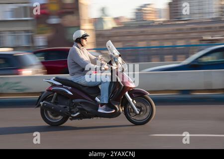 Belgrad, Serbien - 10. Oktober 2024: Reifer Motorradfahrer mit Halbhelm auf einem Motorroller an einem sonnigen Tag auf der Stadtstraße Stockfoto