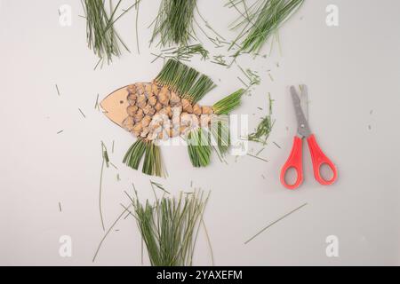 Abstrakter Fisch aus Kiefernnadeln, Schere daneben, grauer Hintergrund, Ansicht von oben nach unten Stockfoto