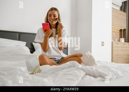 Eine junge Frau schminkt sich, während sie sich bequem auf ihrem Bett entspannt Stockfoto