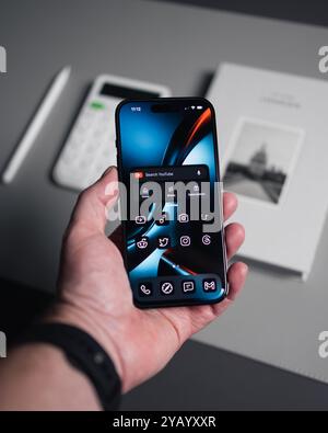LONDON – 15. OKTOBER 2024: Mann hält Platz für schwarzes iPhone Pro in der Hand über Büroarbeitsplatz Stockfoto